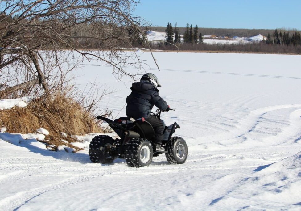 Child Driving His Quad Onto a Frozen Lake A person riding an atv in the snow.